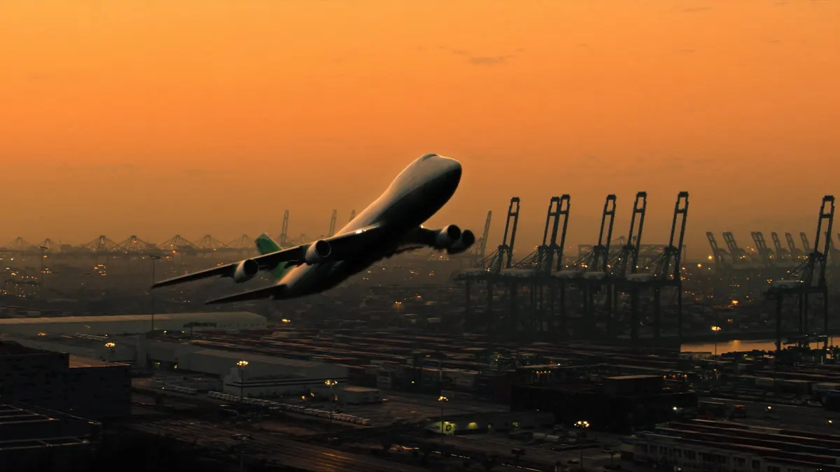 Cargo aircraft over a lit container port at dusk